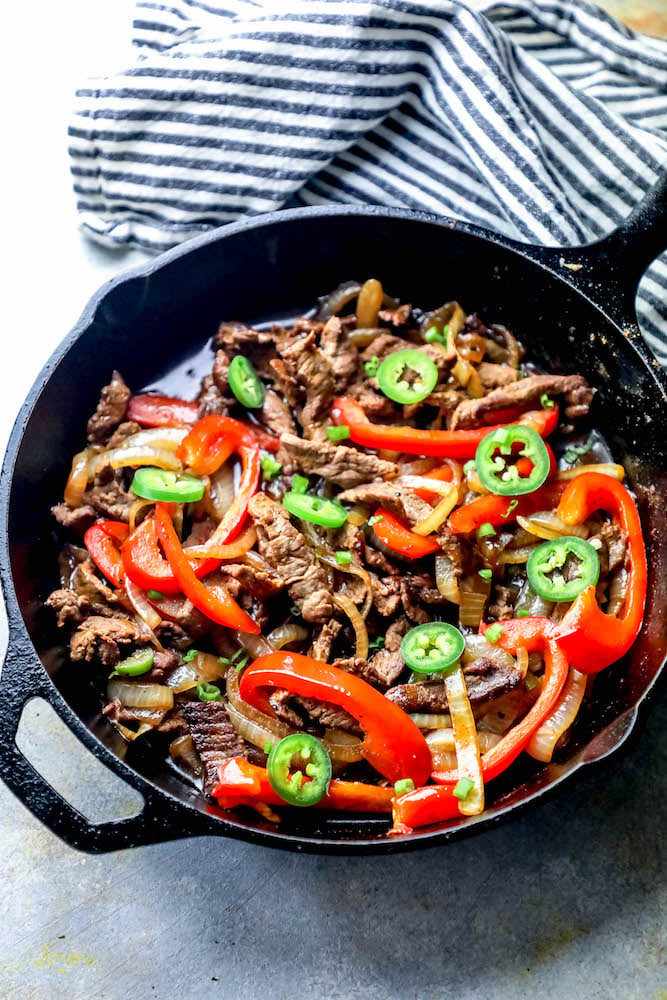 picture of steak fajitas in a cast iron skillet with jalapenos, bell peppers, and onions