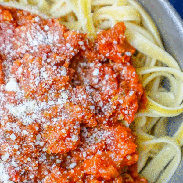 Close-up of fettuccine pasta topped with chunky red pepper marinara sauce and sprinkled with grated Parmesan cheese on a plate.