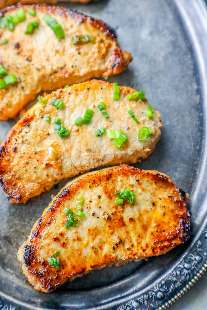 3 baked pork chops on a silver platter with minced chives on top 