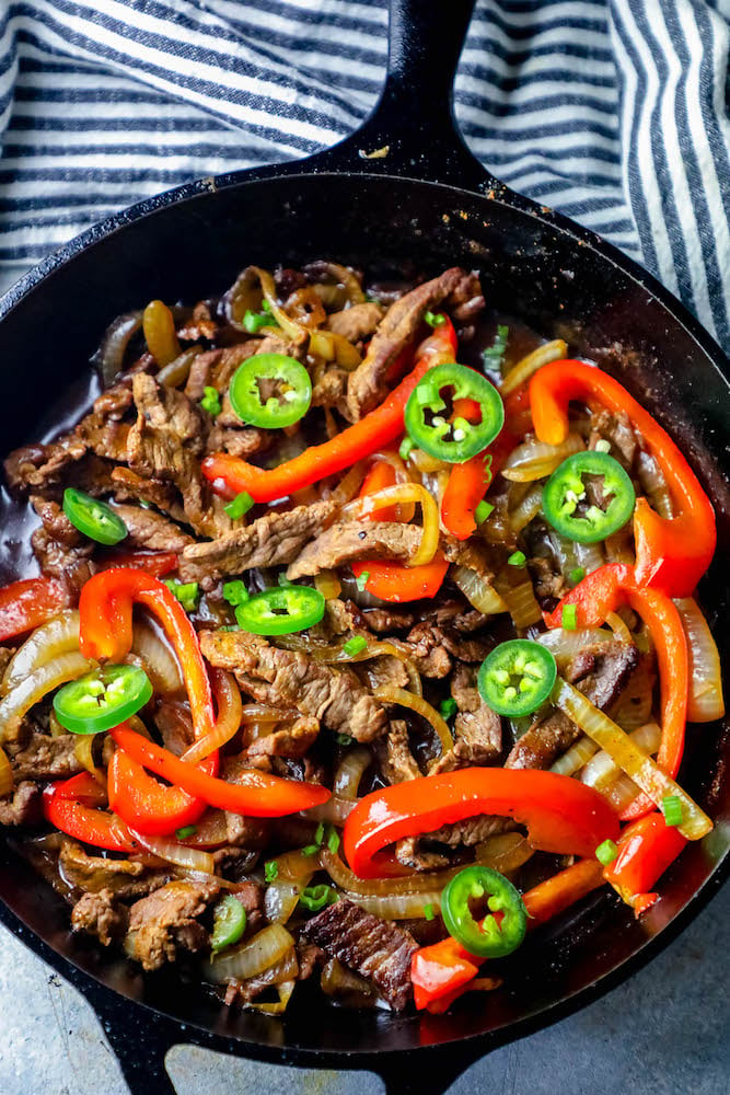 picture of steak fajitas in a cast iron skillet with jalapenos, bell peppers, and onions