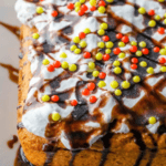 A cake made with box cake mix and pumpkin puree, topped with white frosting, multicolored sprinkles, and chocolate drizzle.