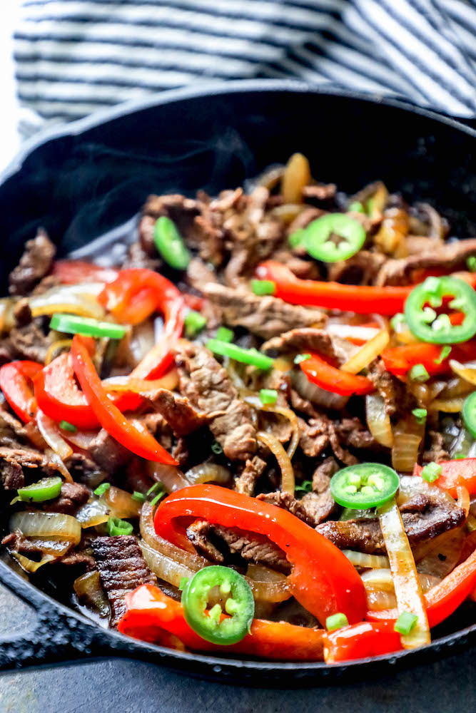 picture of steak fajitas in a cast iron skillet with jalapenos, bell peppers, and onions