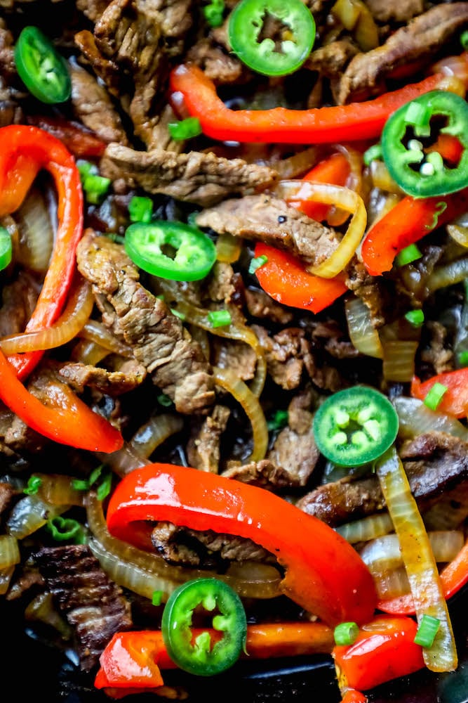 picture of steak fajitas in a cast iron skillet with jalapenos, bell peppers, and onions up close