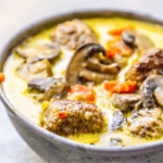 A bowl of creamy one pot meatball and mushroom soup with diced carrots and a yellow broth.