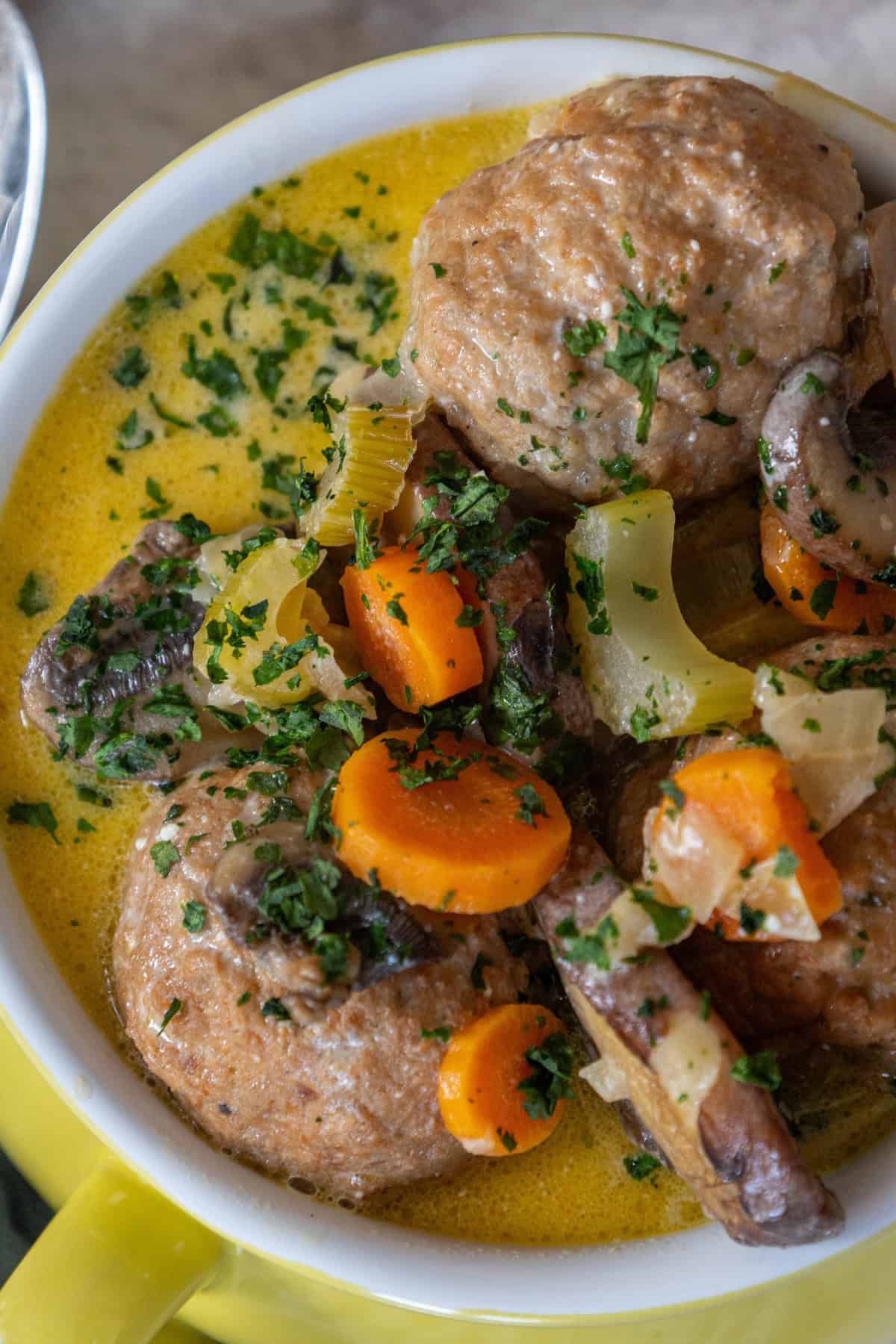 A delightful bowl of meatball soup featuring a keto-friendly mix of sliced carrots, celery, mushrooms, and herbs in a luscious yellow broth. This one-pot creamy meatball soup is both hearty and satisfying for any meal.