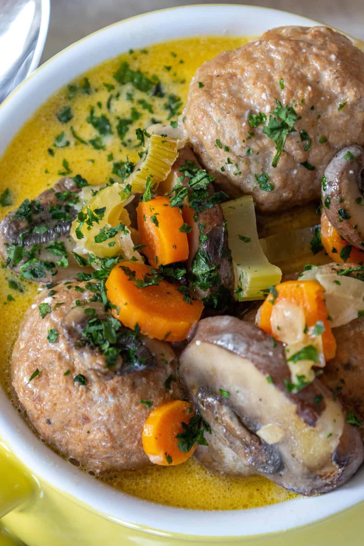 A bowl of one pot creamy meatball soup with tender carrots, mushrooms, and a garnish of chopped parsley swimming in a luscious broth.