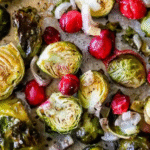 Baked brussels sprouts with cranberries and sliced onions on a baking sheet, seasoned with pepper and herbs, make a flavorful side dish.