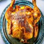 Whole roasted chicken with browned, seasoned skin served on an ornate silver platter—this dish is inspired by a One Pot Easy Cajun Whole Roasted Chicken Recipe, featuring flavorful cajun butter chicken prepared to perfection, ideal for making in a traditional dutch oven.
