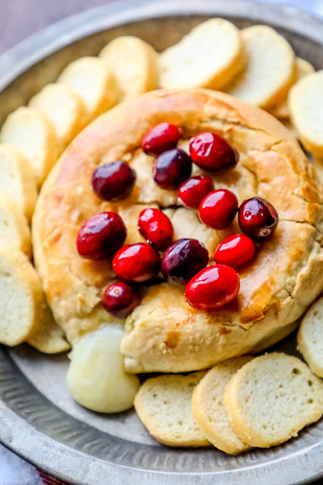 baked brie with cranberries on top oozing out of the puff pastry
