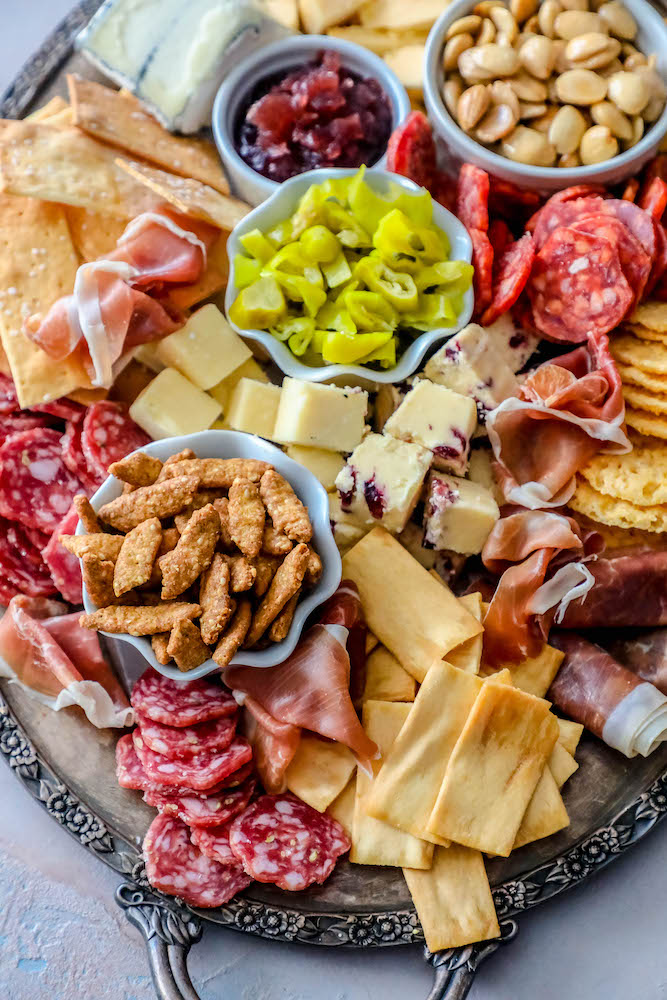 sliced cheeses, meats, nuts, and crackers laid out on a tray. 