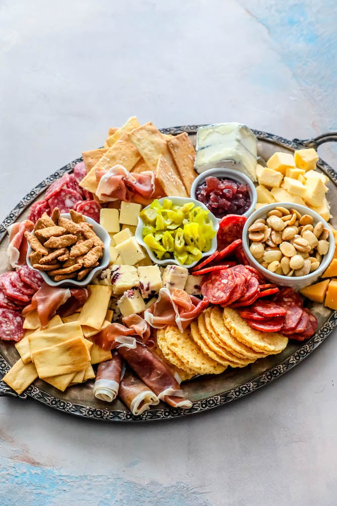 sliced cheeses, meats, nuts, and crackers laid out on a tray. 