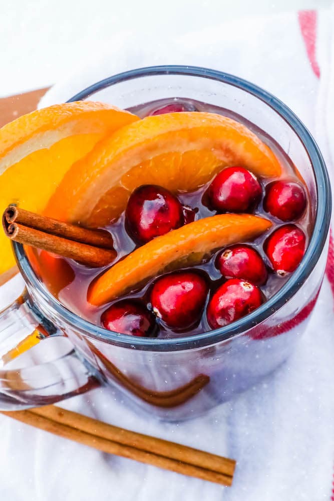 picture of vin chaud in a clear mug with slices of orange and cranberries with cinnamon sticks