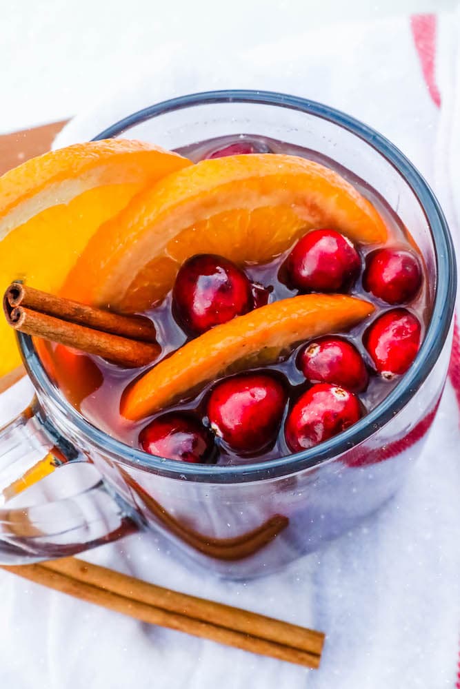 cider in a clear mug with slices of orange and cranberries with cinnamon sticks