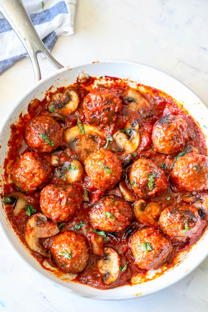 skillet filled with meatballs in marinara sauce with mushrooms and parsley