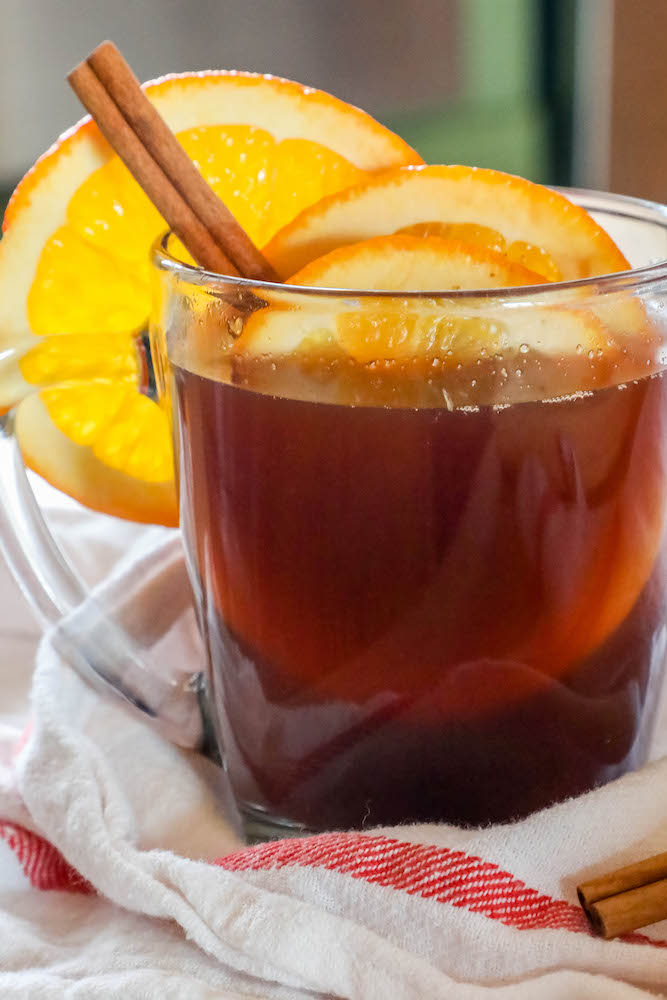 picture of vin chaud in a clear mug with slices of orange and cranberries with cinnamon sticks