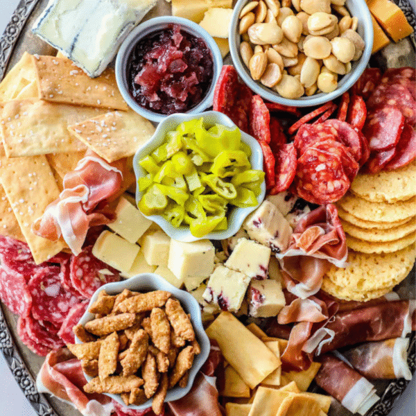 An easy cheese plate featuring assorted cheeses, cured meats, crackers, nuts, pickled peppers, candied nuts, and a small bowl of chutney—perfect for any gathering.
