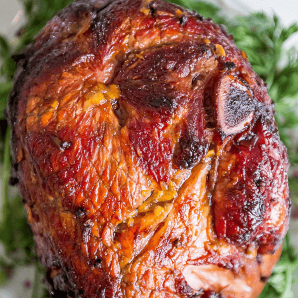 Roasted ham with a caramelized glaze, inspired by a classic glazed ham recipe, surrounded by green garnish, shown close-up on a white plate.
