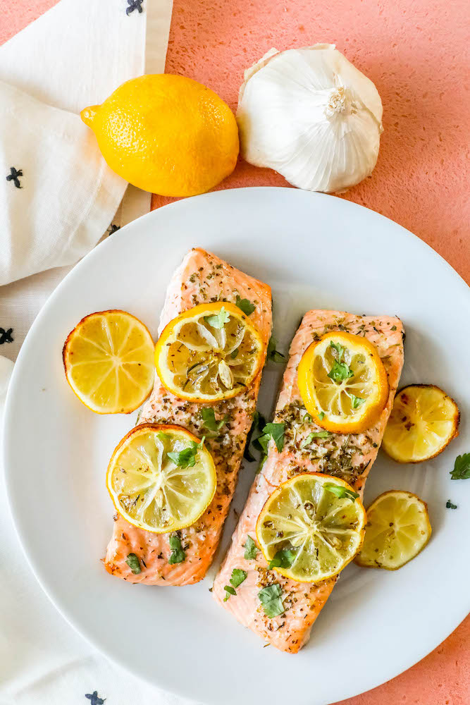 salmon filets with lemon slices, garlic and herbs on top on a white plate