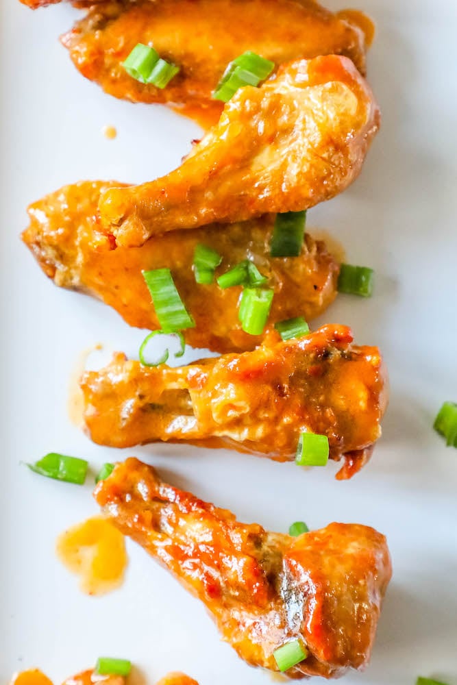 chicken wings on a white plate with sliced green onion on top 