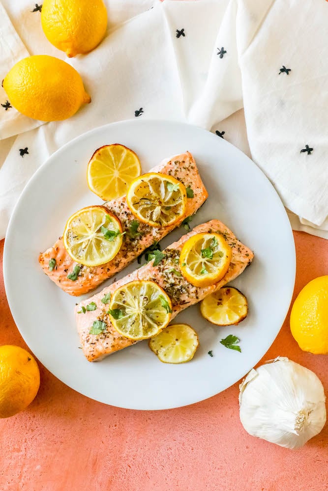 salmon filets with lemon slices, garlic and herbs on top on a white plate