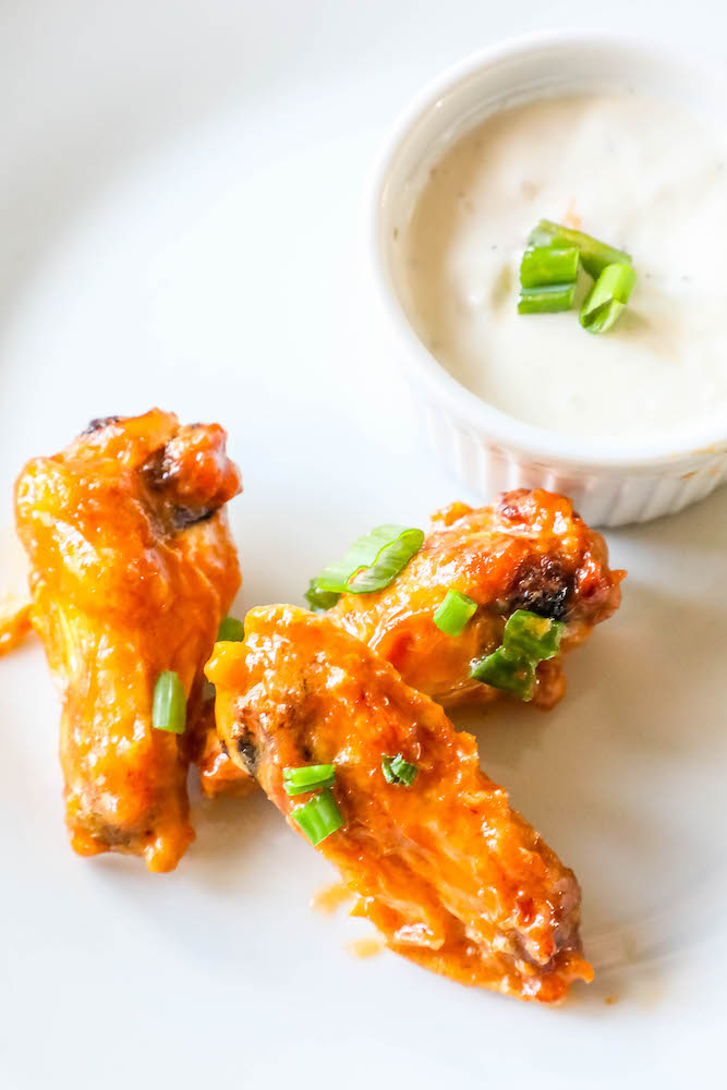 three chicken wings on a white plate with a bowl of ranch dressing 