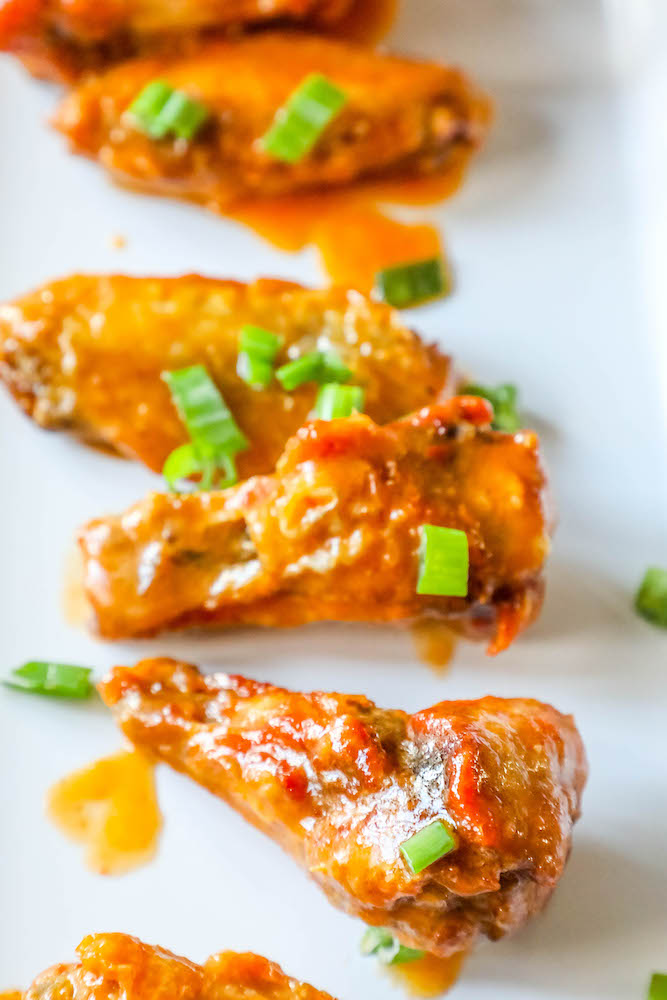 six chicken wing pieces on a plate covered in sauce topped with sliced green onions