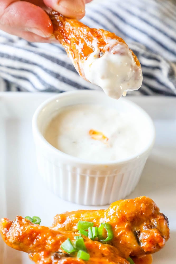 a hand holding a chicken wing dipped in ranch dressing