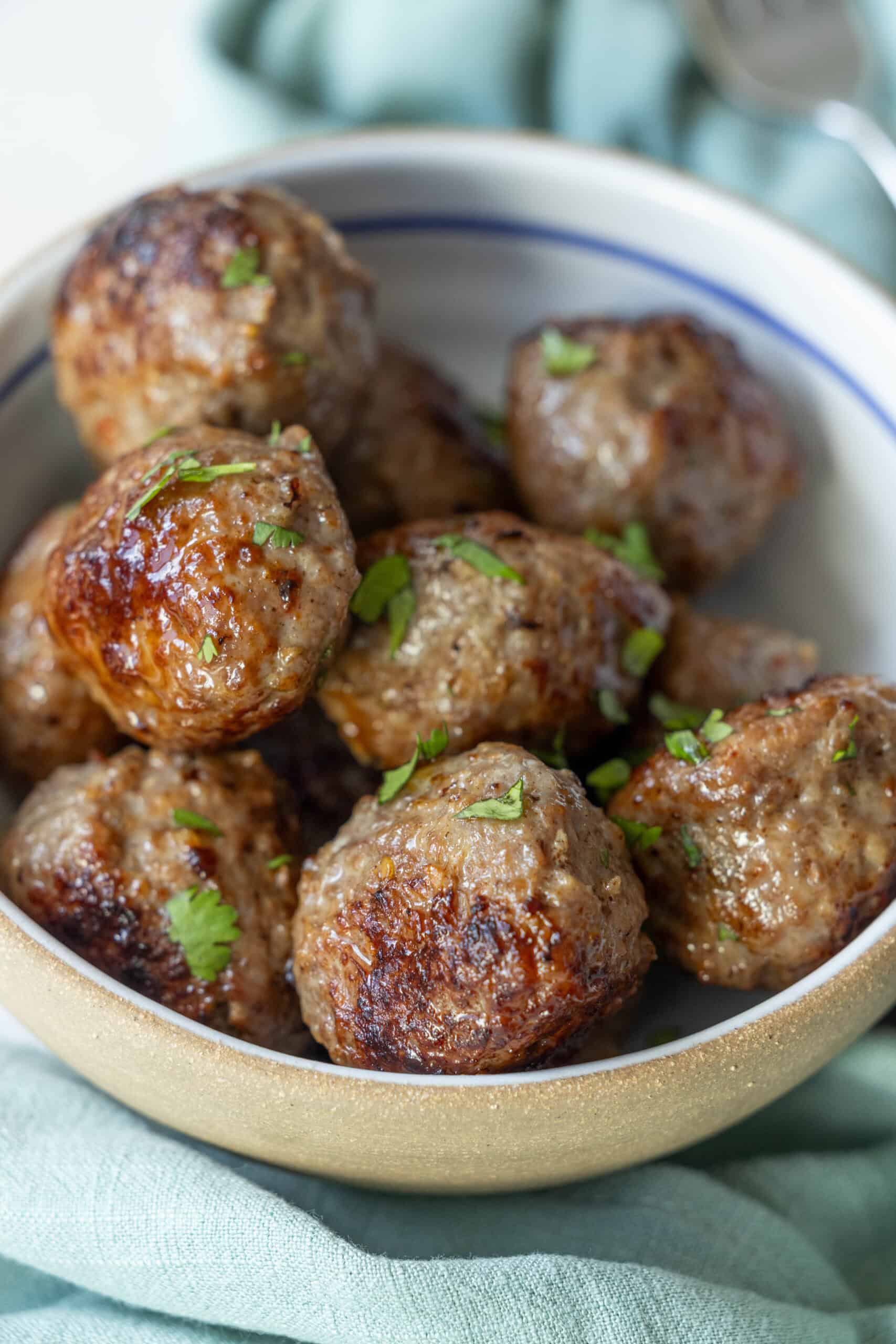 A bowl filled with several browned and seasoned air fried meatballs garnished with chopped herbs.