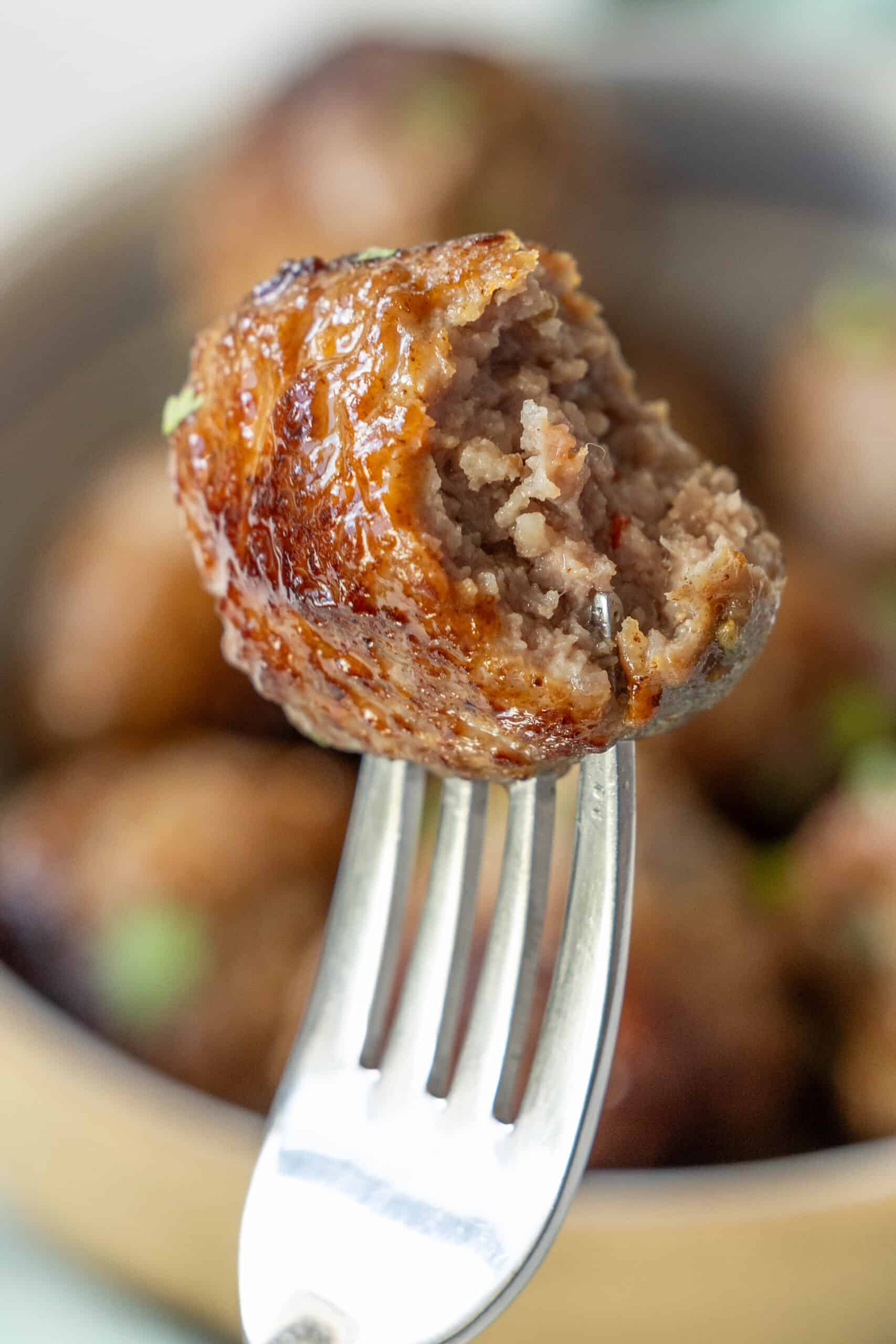 A fork holds a partially bitten air fried meatball, with more meatballs visible in the background.