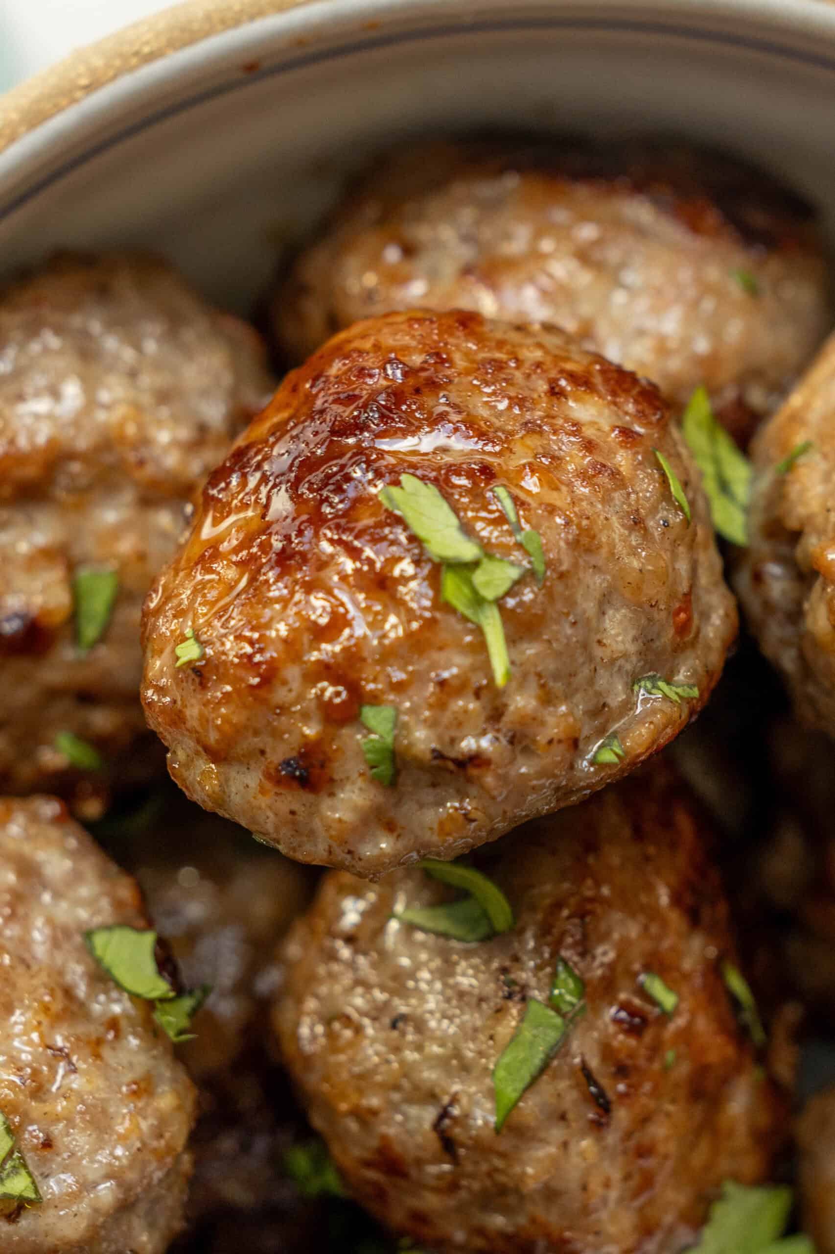 Close-up of a bowl filled with air fried meatballs, garnished with chopped parsley. This easy meatballs recipe results in deliciously cooked meatballs that are both crispy and tender.