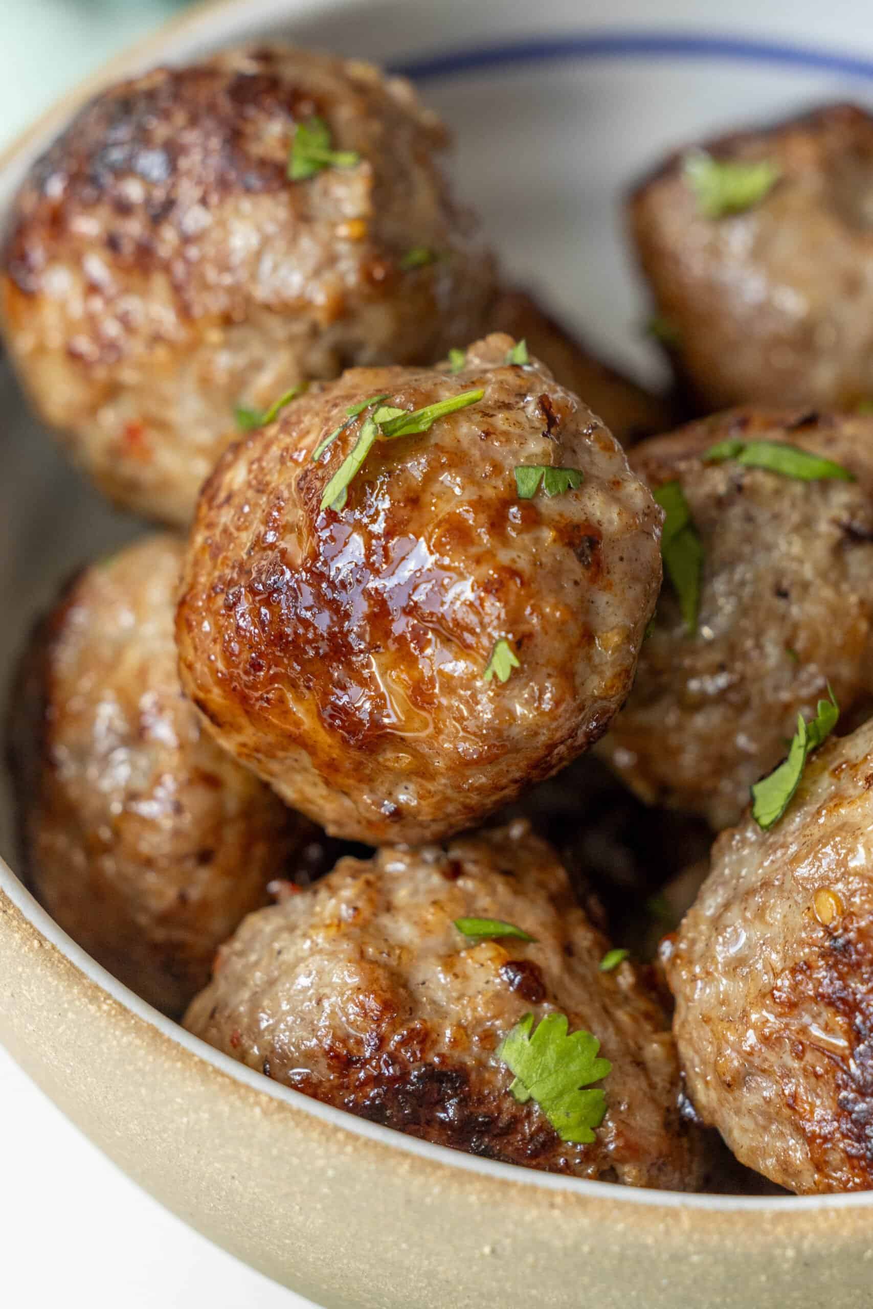 A close-up of air-fried meatballs garnished with chopped herbs in a bowl.