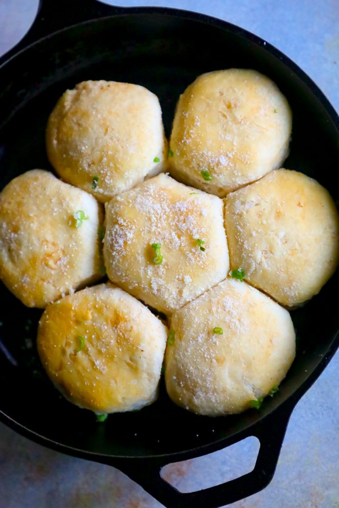 seven dinner rolls in a cast iron skillet with parmesan cheese and green onions. 