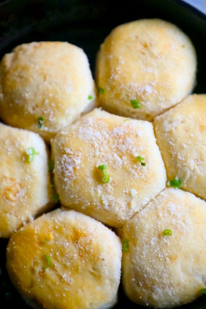 seven dinner rolls in a cast iron skillet with parmesan cheese and green onions. 