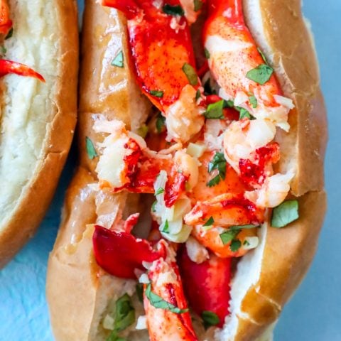 Two lobster hot dogs on a blue plate, featuring a garlic butter naked lobster roll recipe.