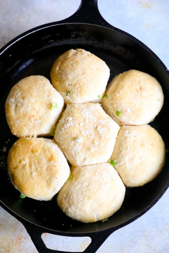 seven dinner rolls in a cast iron skillet with parmesan cheese and green onions. 