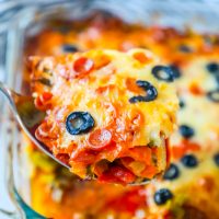 Easy keto cheesy pizza casserole with olives and tomatoes in a glass dish.