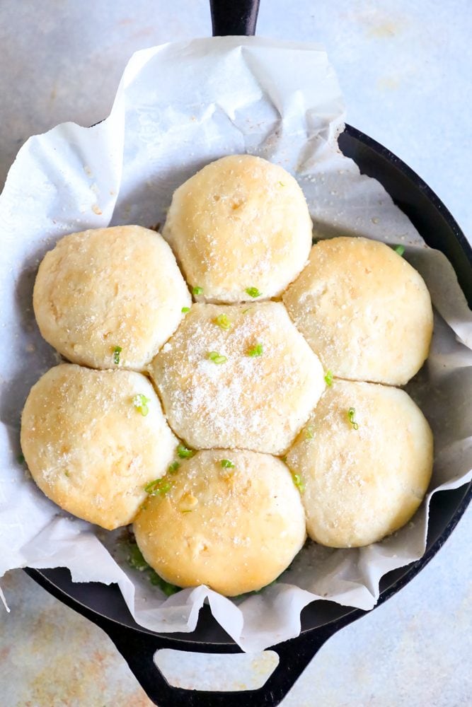 seven dinner rolls in a cast iron skillet with parmesan cheese and green onions. 