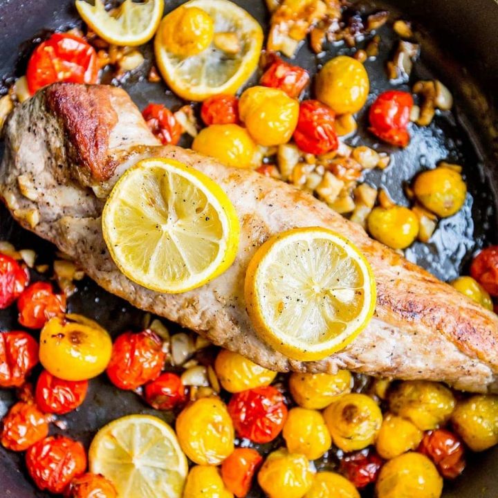 pork with lemon on it in a pan with tomatoes and garlic.
