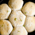 Top view of garlic butter knots sprinkled with parmesan cheese and herbs in a black pan.