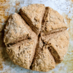 A round loaf of whole-grain soda bread is cut into six triangular pieces on a baking tray.