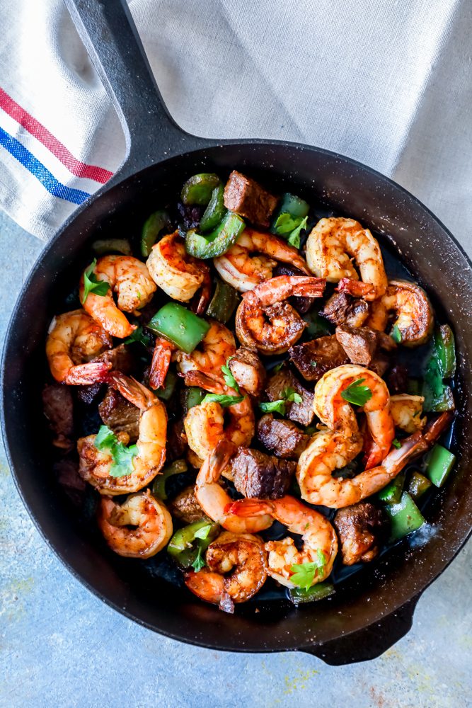shrimp, steak, and spices, parsley all over it in skillet