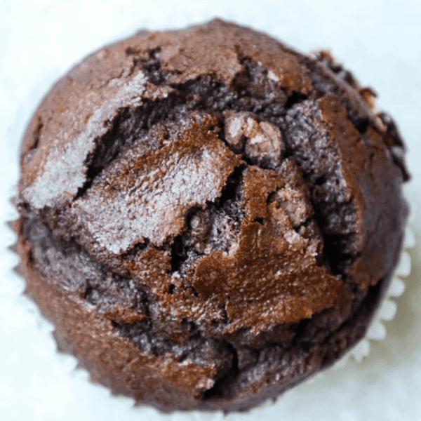 Close-up of a freshly baked double chocolate chunk muffin with a cracked, textured top, viewed from above.