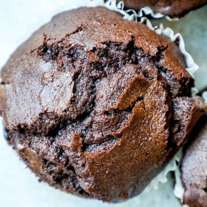 A close up of jumbo chocolate muffins on a white surface.