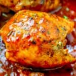 A close-up of golden-brown chicken thighs glazed with spicy, herb-infused sauce in a skillet. This keto chicken thigh skillet dinner features visible herbs and a glossy finish, nestled in thick red sauce for an irresistible touch.