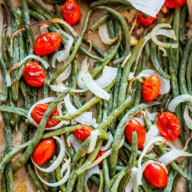 Roasted Green Bean Salad featuring cherry tomatoes and sliced onions, all perfectly arranged on a baking sheet.