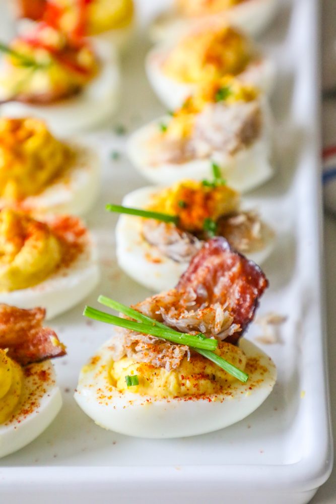 group of deviled egg with chives, crab, and bacon on it
