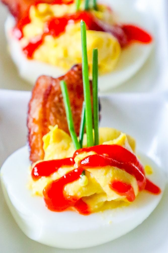 picture of deviled eggs with sriracha, bacon, and chives on a white plate