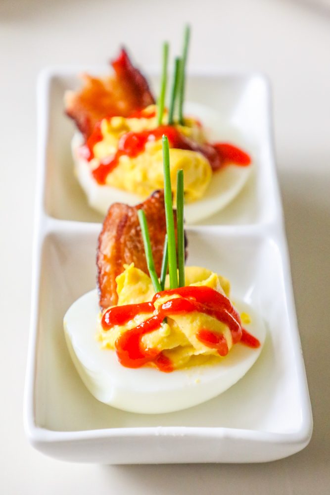 picture of deviled eggs with sriracha, bacon, and chives on a white plate