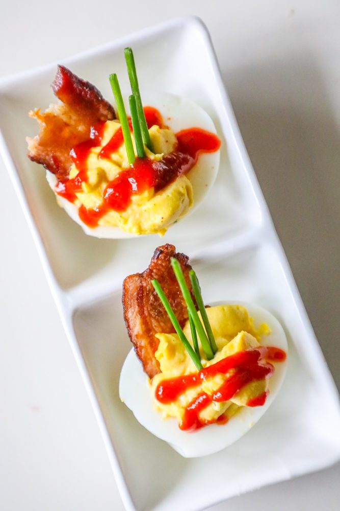 picture of deviled eggs with sriracha, bacon, and chives on a white plate