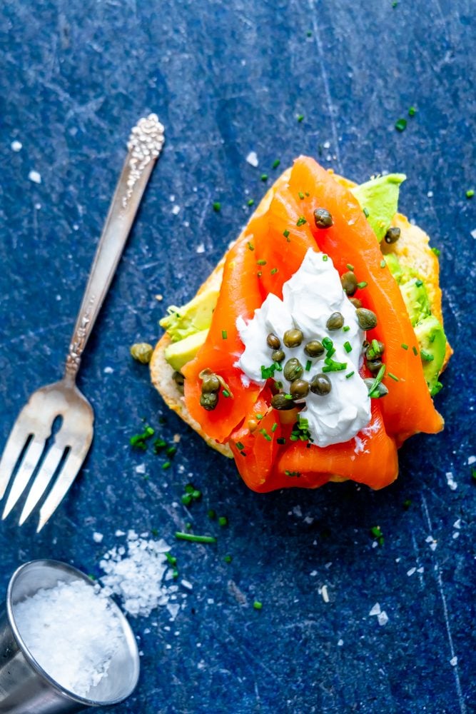 piece of bread with avocado, salmon, creamy, capers, and chives on it